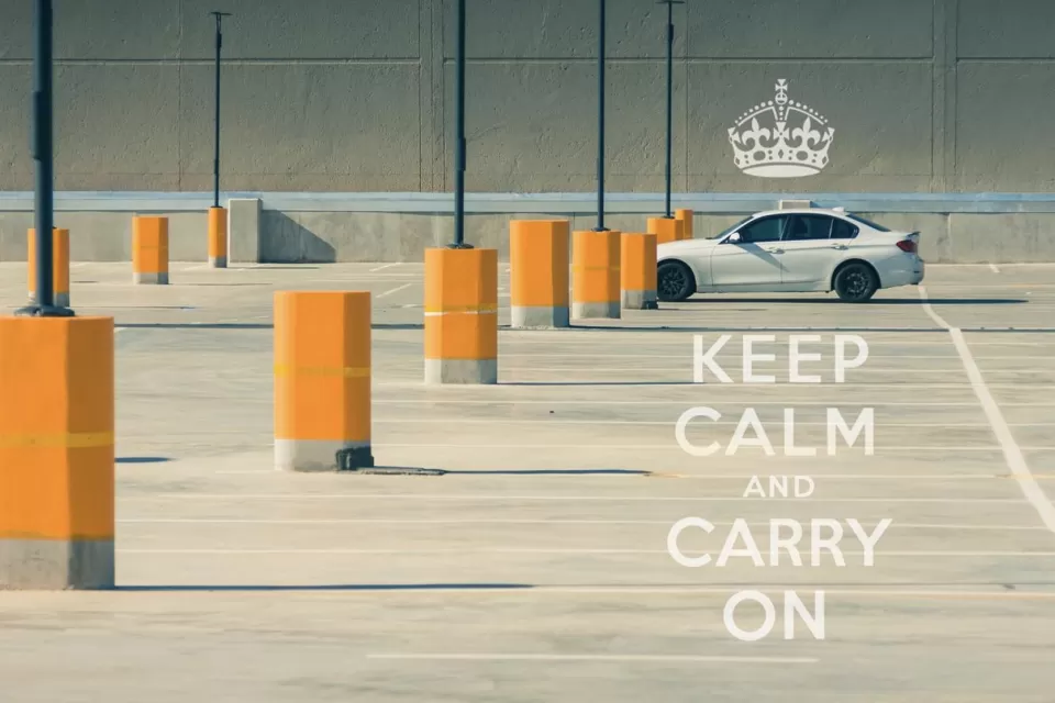 A single car in an empty parking lot full of only bright yellow bollards. A caption on the image reads, "Keep calm and carry on."